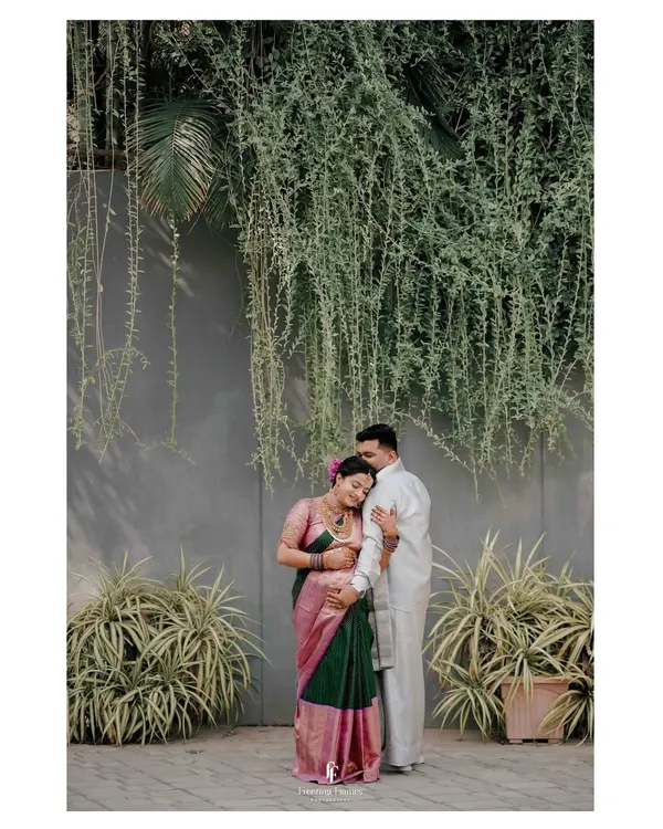 A full-length portrait of an expecting couple against a modern wall with hanging greenery. This image showcases how I blend contemporary backdrops with traditional maternity attire for a unique look.