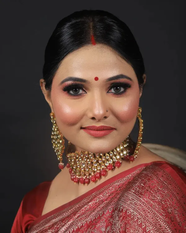 A classic and elegant party makeup look on a model in a red Banarasi saree. The makeup features a flawless base, sharp winged eyeliner, and a complementary red lip for a timeless finish.