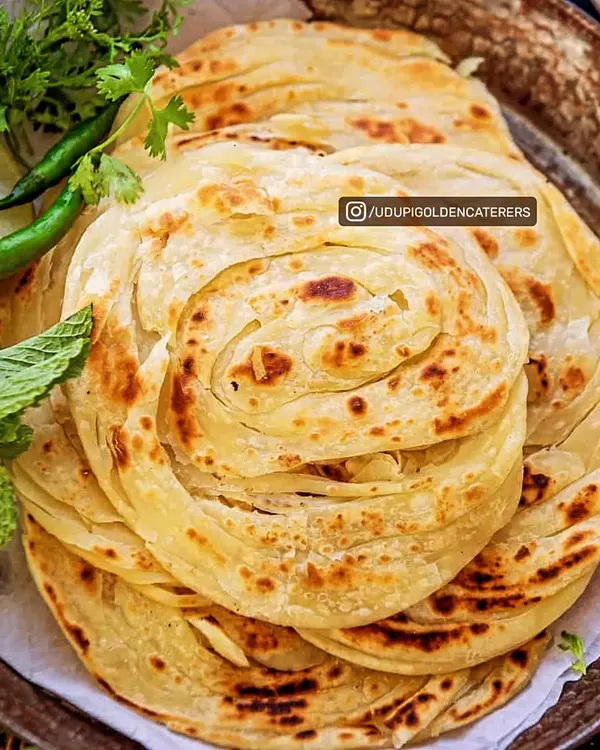 A stack of freshly made Kerala Parottas, showcasing their intricate, flaky layers. These are cooked live on a tawa, ensuring each guest experiences their soft, chewy, and crispy texture.