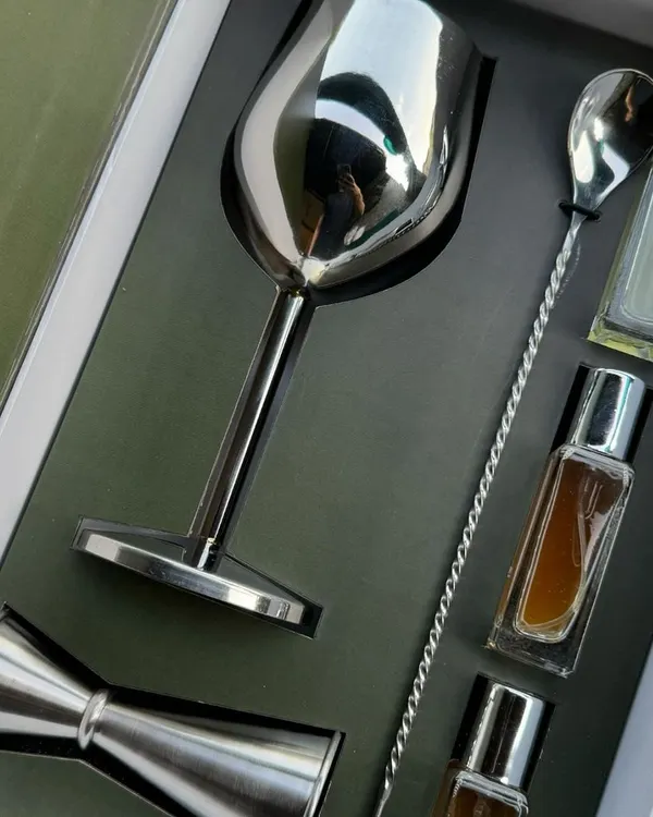 A sleek, modern cocktail kit curated for the launch of One8's special cocktail edition. This PR box features a metallic finish wine goblet, a peg measure, a bar spoon, and custom-branded cocktail mixers, all nested in a sophisticated dark green and silver box.