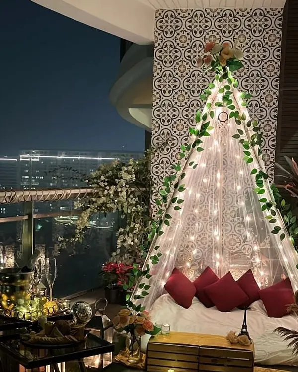 A breathtaking proposal setup on a high-rise balcony. The cabana is adorned with green vines and fairy lights, creating a romantic hideaway with a city skyline view.