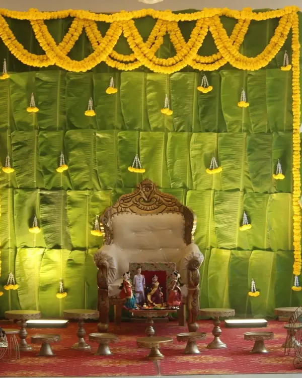 A traditional Seemantham decor featuring a backdrop made entirely of fresh banana leaves, adorned with marigold garlands.