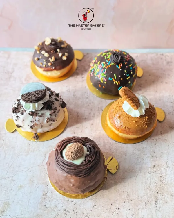 An assortment of our golden, fluffy Bomboloni, also known as filled donuts. This lineup includes flavors like Ferrero Rocher, Oreo, Lotus Biscoff, classic chocolate sprinkle, and hazelnut chocolate.