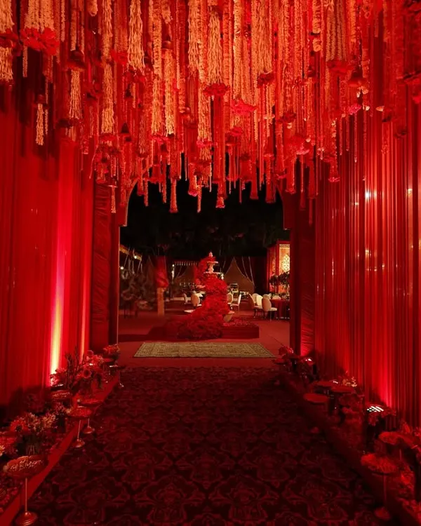 This grand crimson aisle, draped in flowing curtains and adorned with cascading floral chandeliers, was designed to create a regal and immersive welcome.