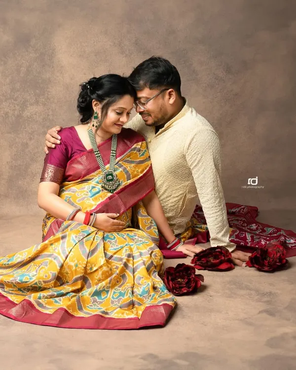 An intimate moment between a couple during their traditional maternity shoot. The rich colors of the saree and the warm studio lighting create a beautiful, classic portrait.