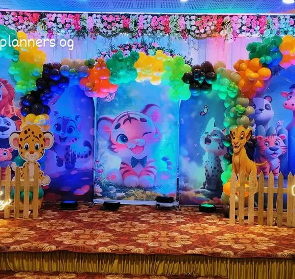 A full view of our vibrant jungle theme party setup in a banquet hall. We use multiple backdrops, a picket fence, and character cutouts to create an immersive safari experience for the little one's first birthday.