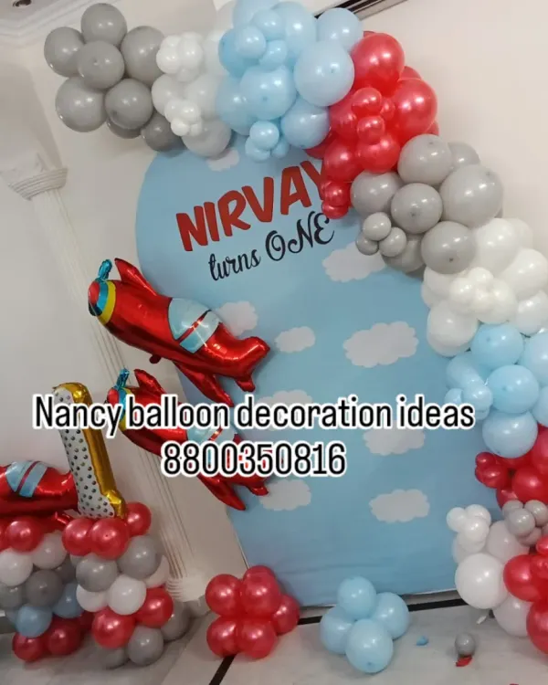 An airplane-themed first birthday decoration for Nirvay. I used a custom-printed backdrop with clouds and created a balloon arch in red, grey, and light blue, adding airplane foil balloons to complete the theme.