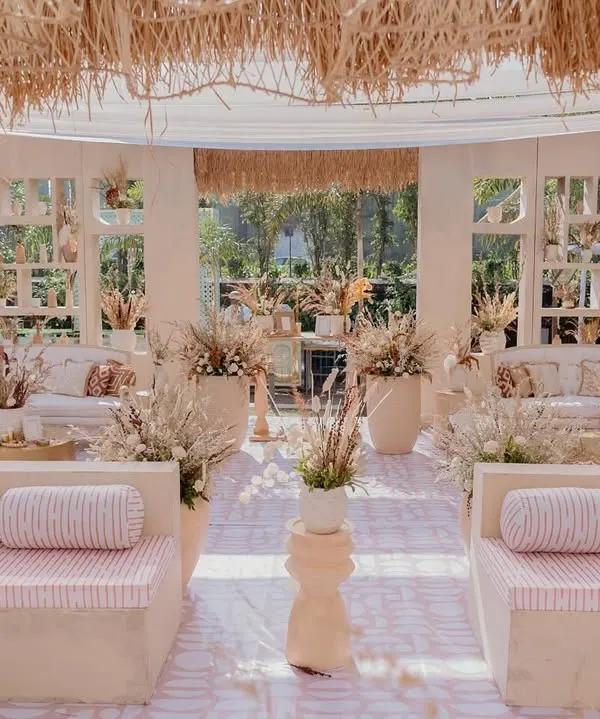 A wide view of the "Desert Oasis" Haldi lounge. The space features custom low seating with striped cushions, a thatched roof canopy, and earthy decor for a relaxed, bohemian vibe.
