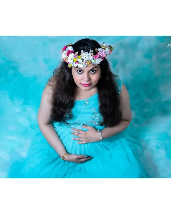 An artistic studio portrait taken from a high angle. The mother-to-be, seated in a sea of blue fabric, looks up at the camera, creating a dramatic and captivating image.