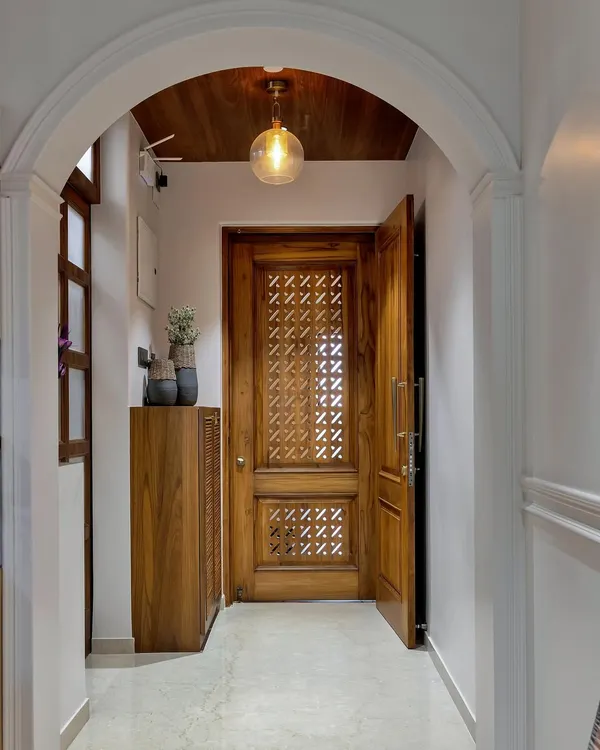 The beauty is in the details. This stunning entryway features an intricately carved wooden door, an arched passage, and warm pendant lighting, creating a grand and welcoming first impression.