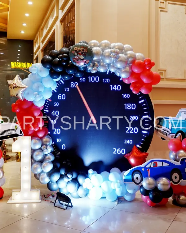 A creative photo opportunity for a car-themed party, featuring a giant speedometer backdrop and car-shaped balloon sculptures.