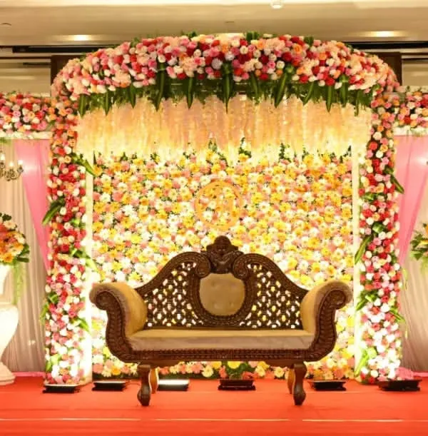 A magnificent floral stage we created for a wedding reception. This design features a dense wall of pink, white, and yellow flowers with hanging floral strings, creating a truly grand backdrop.