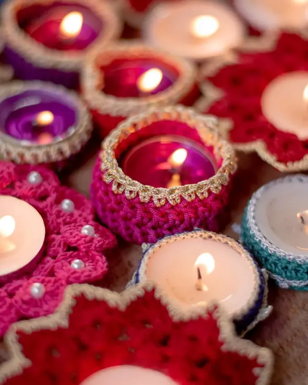 A vibrant collection of our handmade crochet diya holders, lit up to show how they bring a warm, festive glow to any space. This image captures our most popular Diwali items, including pink flower-shaped coasters with pearl beads and colorful tea light jackets.
