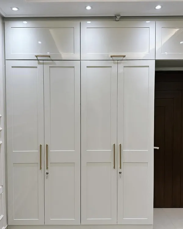 A floor-to-ceiling white wardrobe designed in a modern Victorian style. This piece features classic panelled doors with sleek golden handles and provides ample overhead storage, blending timeless design with practical functionality.