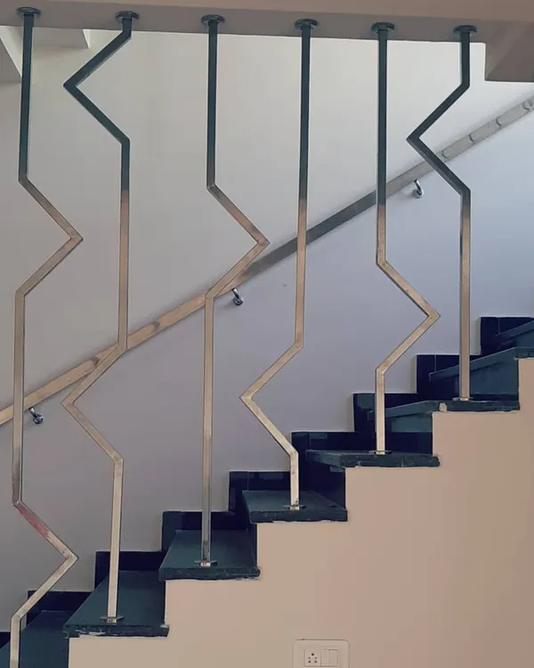 This custom staircase railing features a modern, geometric design made of stainless steel. The zig-zag pattern creates a strong visual line that is both a safety feature and a sculptural element within the home's interior.