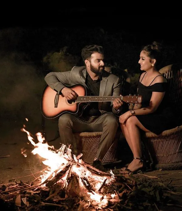 A pre-wedding shoot set against a crackling bonfire at night. The groom plays the guitar for his fiancée, creating a warm, intimate, and cinematic scene perfect for a couple's love story film.