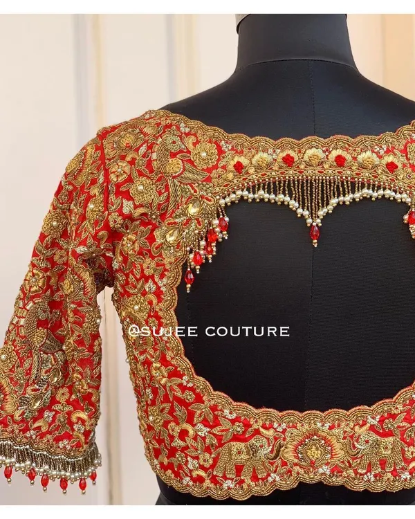 A truly unforgettable statement back. This red bridal blouse features a bold heart-shaped cutout, heavily outlined with gold zardozi and finished with hanging pearl and red bead tassels.