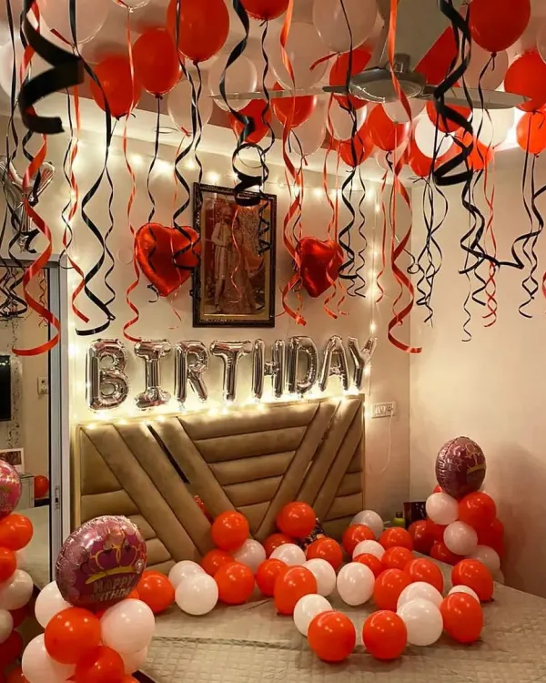 A classic birthday room decoration with red and white balloons covering the ceiling and floor, and 'BIRTHDAY' foil letters above the bed.
