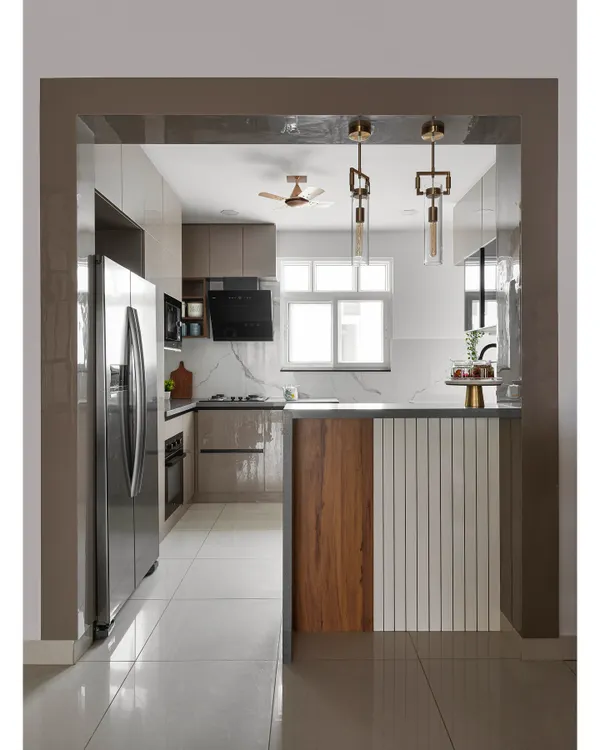 This open-concept kitchen features a pass-through view to the dining area, complete with a breakfast bar. The design uses a mix of wood and white fluted panels on the island, glossy beige cabinets, and a marble-finish backsplash.