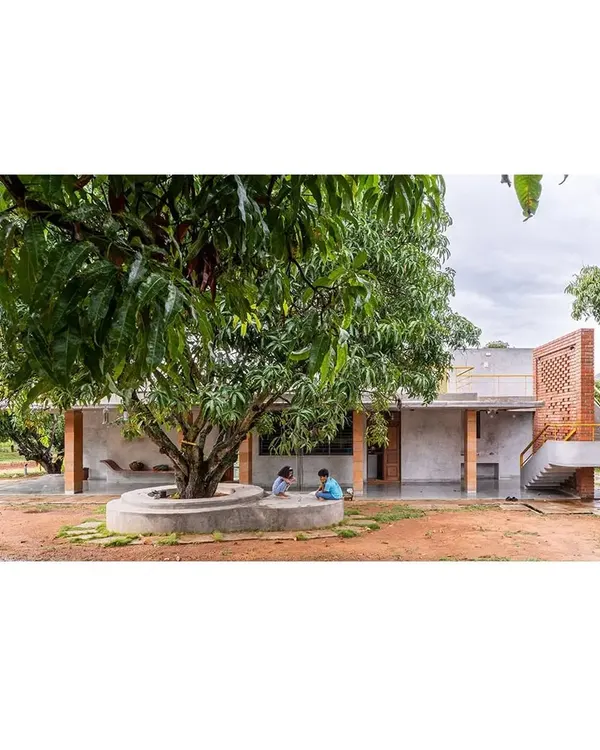 The 'Aamra' residence is designed around a majestic mango tree, which becomes a natural gathering spot. The structure's L-shape form creates a protective embrace around this central feature, integrating the home with the existing orchard.