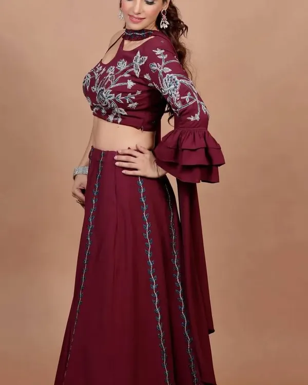 This wine-colored indo-western lehenga features a stylish one-shoulder blouse with bell sleeves and beautiful embroidery. It's a perfect blend of modern trends and ethnic charm.