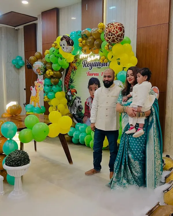 A jungle-themed first birthday party setup, complete with a green and yellow balloon arch, animal cutouts, and a low-lying fog effect for a magical touch.