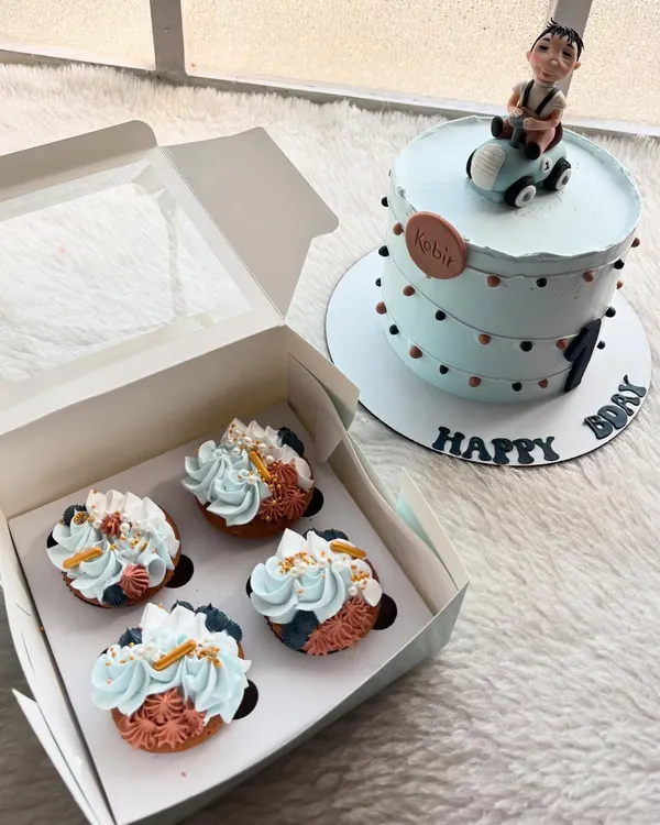 A cute first birthday cake with a fondant caricature of the birthday boy in a car. The order also included matching cupcakes with a blue and coral color scheme.