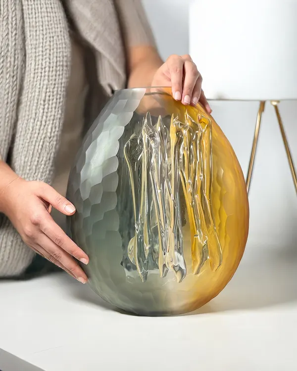 This hand-blown glass vase, with its striking blend of smoky grey and warm amber, is a true conversation starter. Its organic form and unique texture capture the light beautifully, making it a piece of art that transforms any space it inhabits.