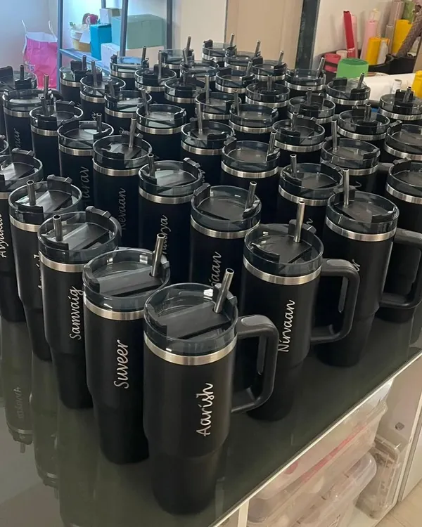 We handle bulk orders with precision and style. This image shows a large batch of personalized black tumblers, each engraved with a name, ready for a corporate event or a large party.