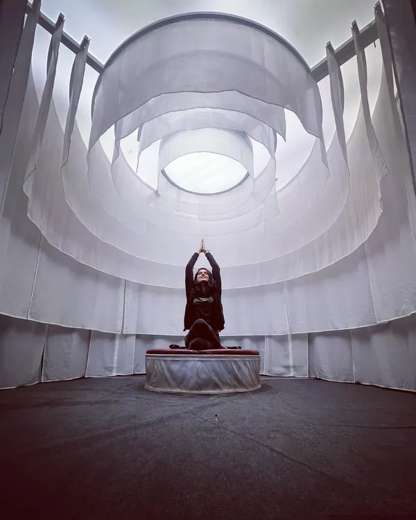 Finding stillness in Gomukhasana, or cow face pose, within a serene meditation space. The circular white drapes create a cocoon-like feeling, perfect for turning your focus inward.