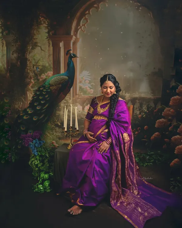A mother-to-be seated in a setting reminiscent of an 18th-century Indian court. The deep purple Kanjivaram saree, the peacock, and the candlelight create a portrait that feels both timeless and divine.
