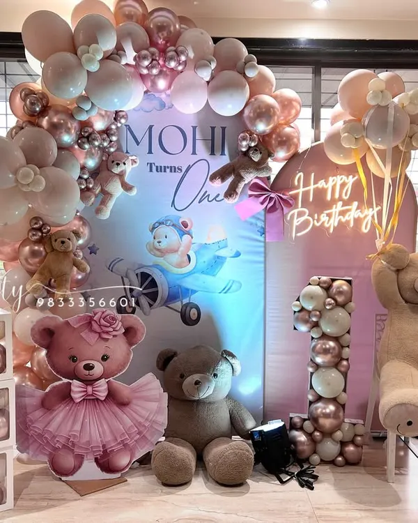 A beautiful teddy bear theme for a first birthday, featuring a soft pink and rose gold color palette. This setup includes a custom backdrop, 'ONE' letter blocks, a balloon-filled marquee number, and a 'Happy Birthday' neon sign.