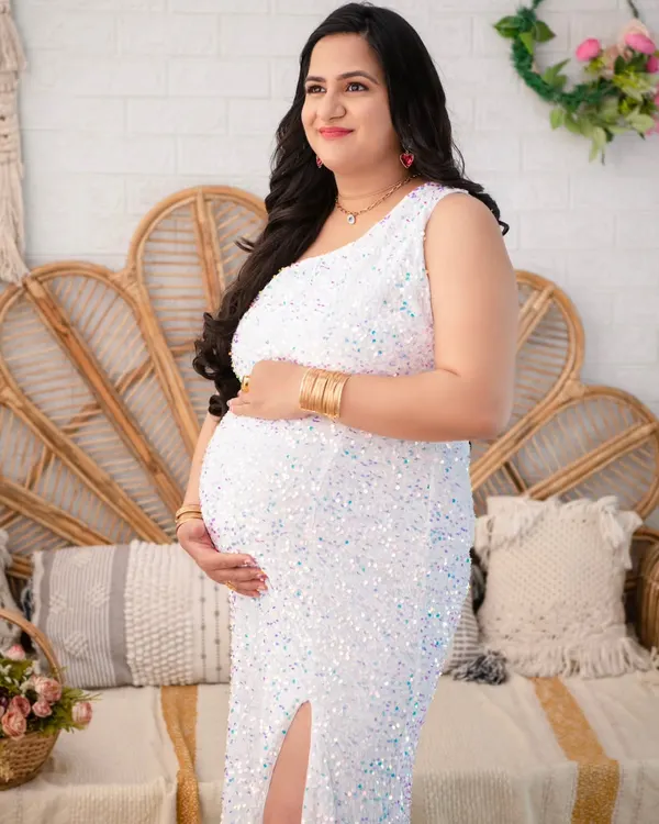 A moment of quiet confidence. Here, the mother-to-be glows in a white sequin mermaid gown, her pose highlighting the beautiful silhouette of pregnancy against our boho-chic studio set.