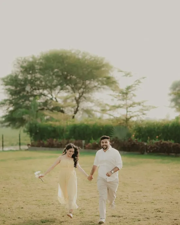 A happy couple runs hand-in-hand through a green field. This candid engagement photo is full of movement and genuine smiles, capturing the pure fun of being together.