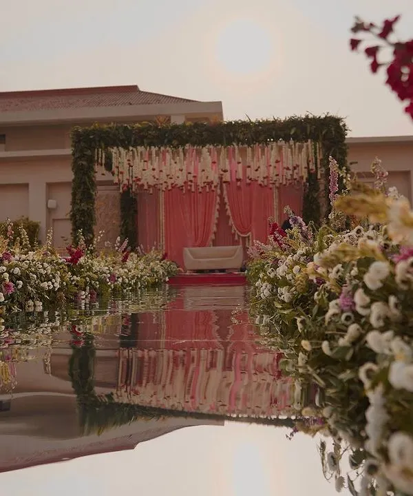 A breathtaking view of a wedding mandap set against the water. We created a floral paradise with a lush aisle and a canopy of greenery, perfectly reflected to create a mirror image of the stunning setup.