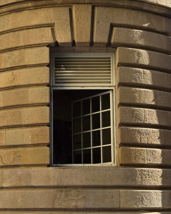A close-up of a window in a stone building in Fort, Mumbai. The play of light and shadow on the gridded pane and louvered shutter is just perfect.