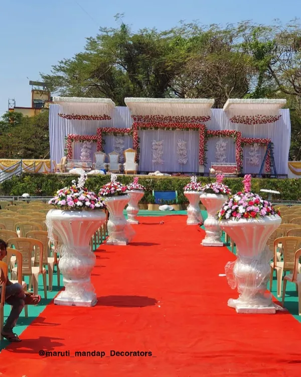 This is the kind of grand wedding stage I can create for your big day. I set up a wide, elegant stage with beautiful floral arrangements and a clean white backdrop, complete with a red carpet aisle lined with decorative flower pots for a royal entrance.