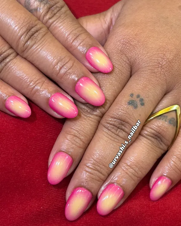 A beautiful and soft ombré manicure. The colors seamlessly blend from a sunny yellow at the base to a vibrant pink at the tips, creating a warm, sunset-inspired gradient with a glossy finish.