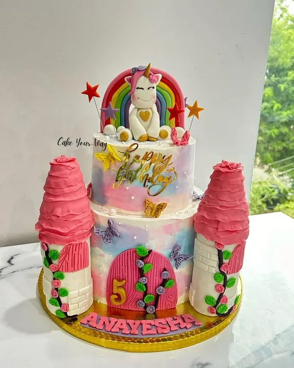A magical unicorn castle cake for a 5th birthday. This two-tier design features buttercream towers, a whimsical unicorn, and a rainbow, creating a complete fairytale scene.