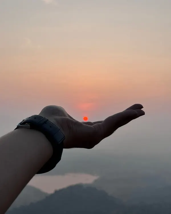 A creative shot of a trekker holding the rising sun in their palm at Uttari Betta.