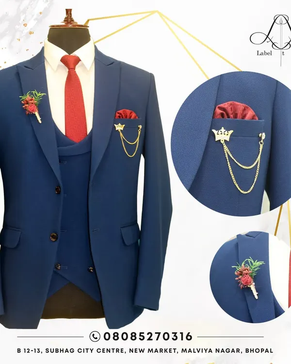 A classic navy blue three-piece suit, perfectly styled with a bold red tie and matching pocket square. The details, like the floral lapel pin and crown brooch, show how we can personalize a timeless look for a wedding or formal event.