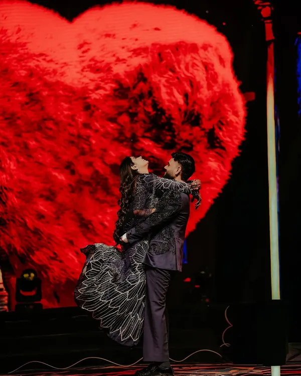 A classic romantic pose on the Sangeet stage. The groom lifts his bride against a giant, glowing red heart, creating a dramatic and iconic shot that’s perfect for a night of celebration.