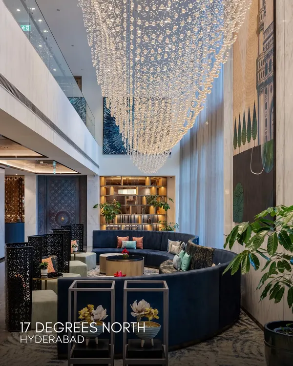 The grand lobby of 17 Degrees North in Hyderabad, where a cascading crystal chandelier descends through a double-height space. The design features a curved deep blue sofa and bespoke art, creating a luxurious and welcoming arrival experience inspired by the city's royal heritage.