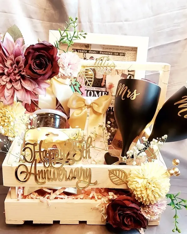 Celebrating a 25th anniversary with this grand hamper. It includes "Mr" and "Mrs" glasses, a vintage photo frame, and other personalized items, all beautifully arranged in a wooden crate.