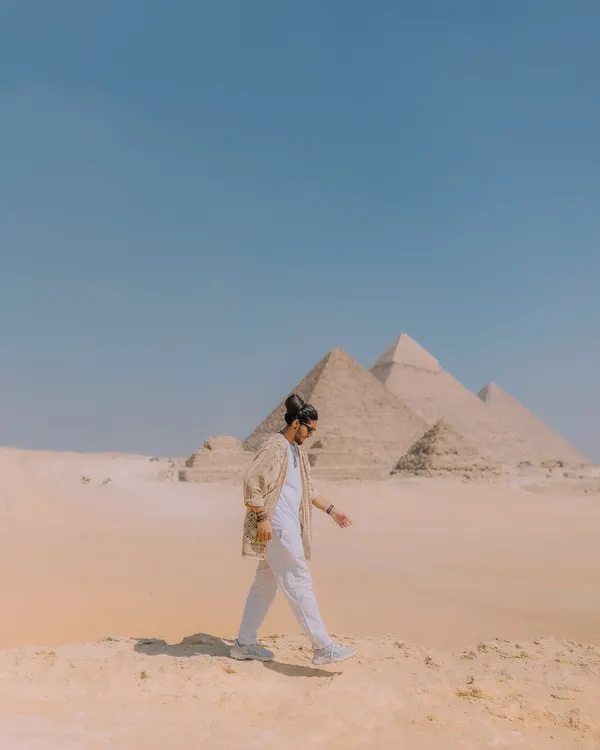 Walking across the sands of Giza with the pyramids in the distance. This wide shot captures the immense scale of the landscape and the feeling of being a small part of a grand history.