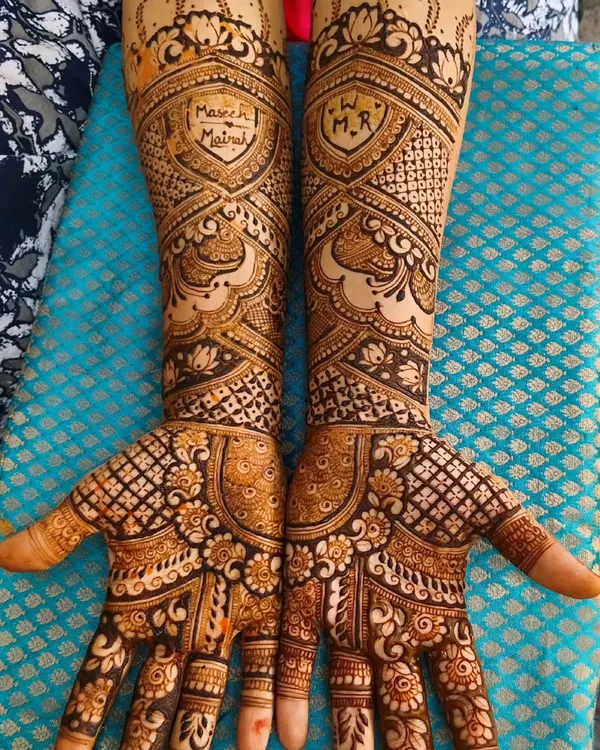 This bridal design is a testament to timeless elegance, featuring intricate shield motifs with custom initials. The combination of delicate floral patterns and geometric jaali work creates a rich, balanced look perfect for a bride.