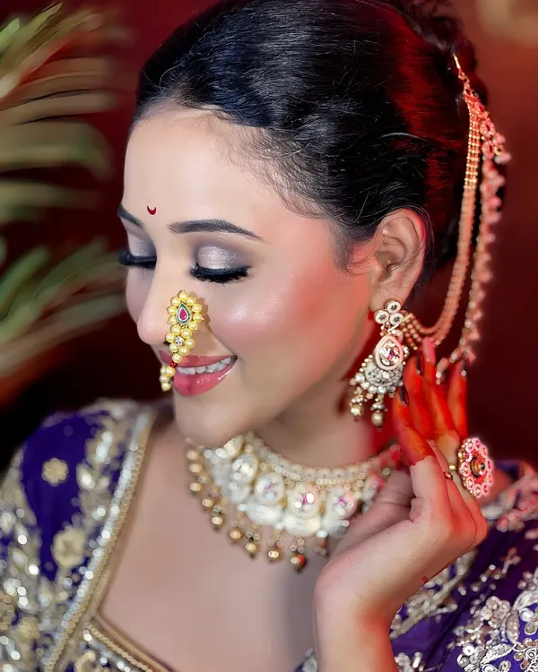 A radiant Maharashtrian bride, showcasing a flawless, glowing makeup look. The intricate Kundan and pearl jewellery set, including the traditional nath and choker, is available for rent to complete your perfect wedding day style.