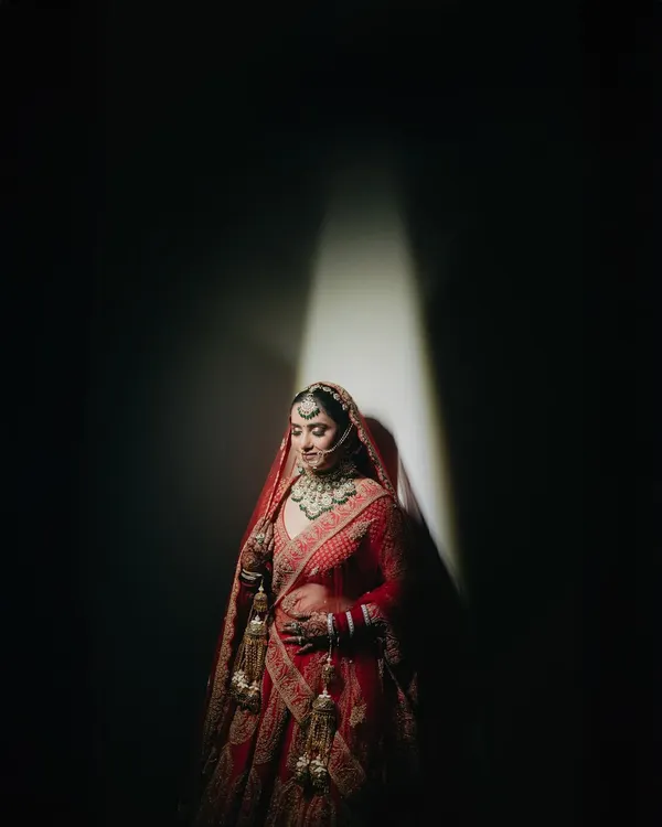 A stunning bridal portrait of Shreya, using a single beam of light to create a dramatic, high-fashion effect. This technique highlights her features and the richness of her red lehenga, turning a photo into a piece of art.