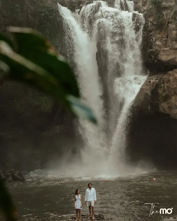 An epic shot of a couple standing before a majestic waterfall in Bali. This image captures the power of nature and the spirit of adventure, showing the scale of the landscape and the couple's place within it.
