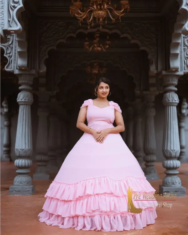This light pink ball gown features a full skirt with tiered ruffles, creating a soft, romantic, and princess-like silhouette. It's perfect for grand, architectural settings.